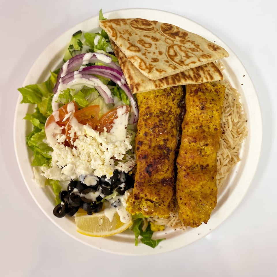 A plate of chicken kabobs with rice, salad, feta, olives, red onion, and pita bread.